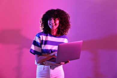 Photo of Beautiful young woman with laptop on color background in neon lights