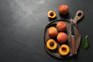 Photo of Delicious juicy peaches, leaf and knife on black textured table, flat lay. Space for text