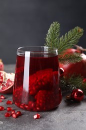 Aromatic Sangria drink in glass, Christmas decor and pomegranate grains on grey textured table, closeup