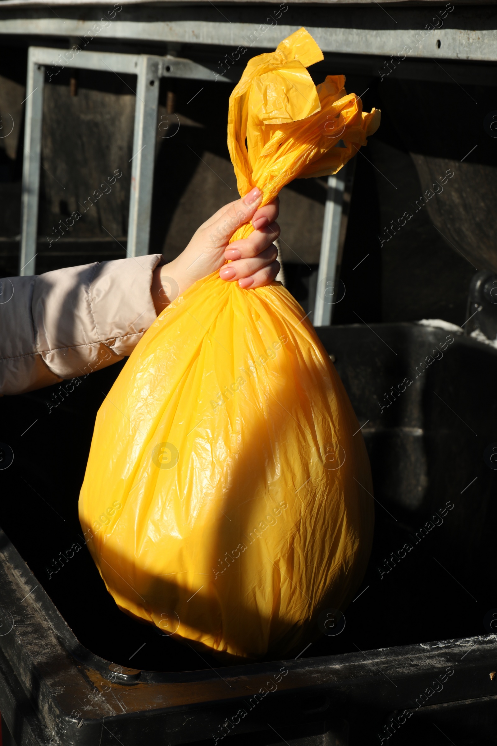 Photo of Woman throwing trash bag full of garbage in bin outdoors, closeup