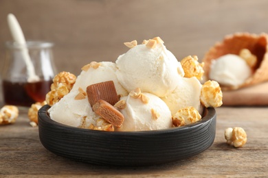 Photo of Plate of delicious ice cream with caramel candies and popcorn on wooden table, closeup