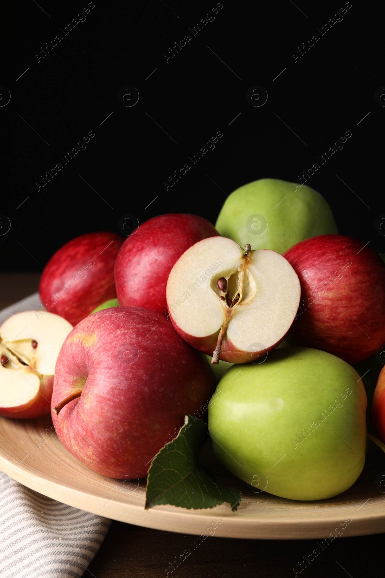 Photo of Plate with fresh ripe apples and leaf on wooden table against dark background, closeup