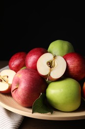 Photo of Plate with fresh ripe apples and leaf on wooden table against dark background, closeup