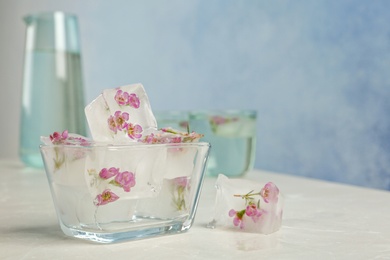 Photo of Bowl with floral ice cubes on table. Space for text