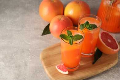 Photo of Tasty freshly made grapefruit juice, fruits and mint on light grey table, space for text