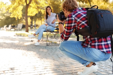 Photo of Young male photographer taking photo of model with professional camera in park