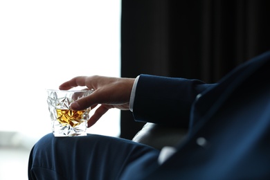 Young man with glass of whiskey indoors, closeup