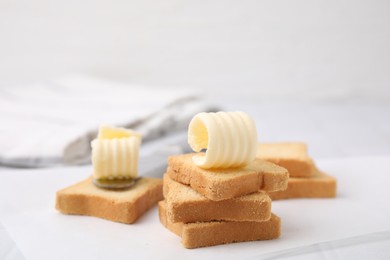 Tasty butter curls, knife and pieces of dry bread on white table, closeup