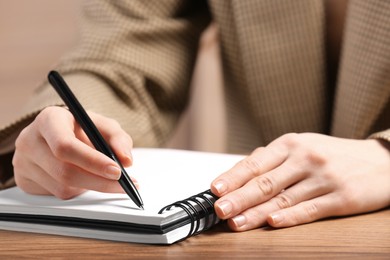 Photo of Woman writing in notebook at wooden table, closeup