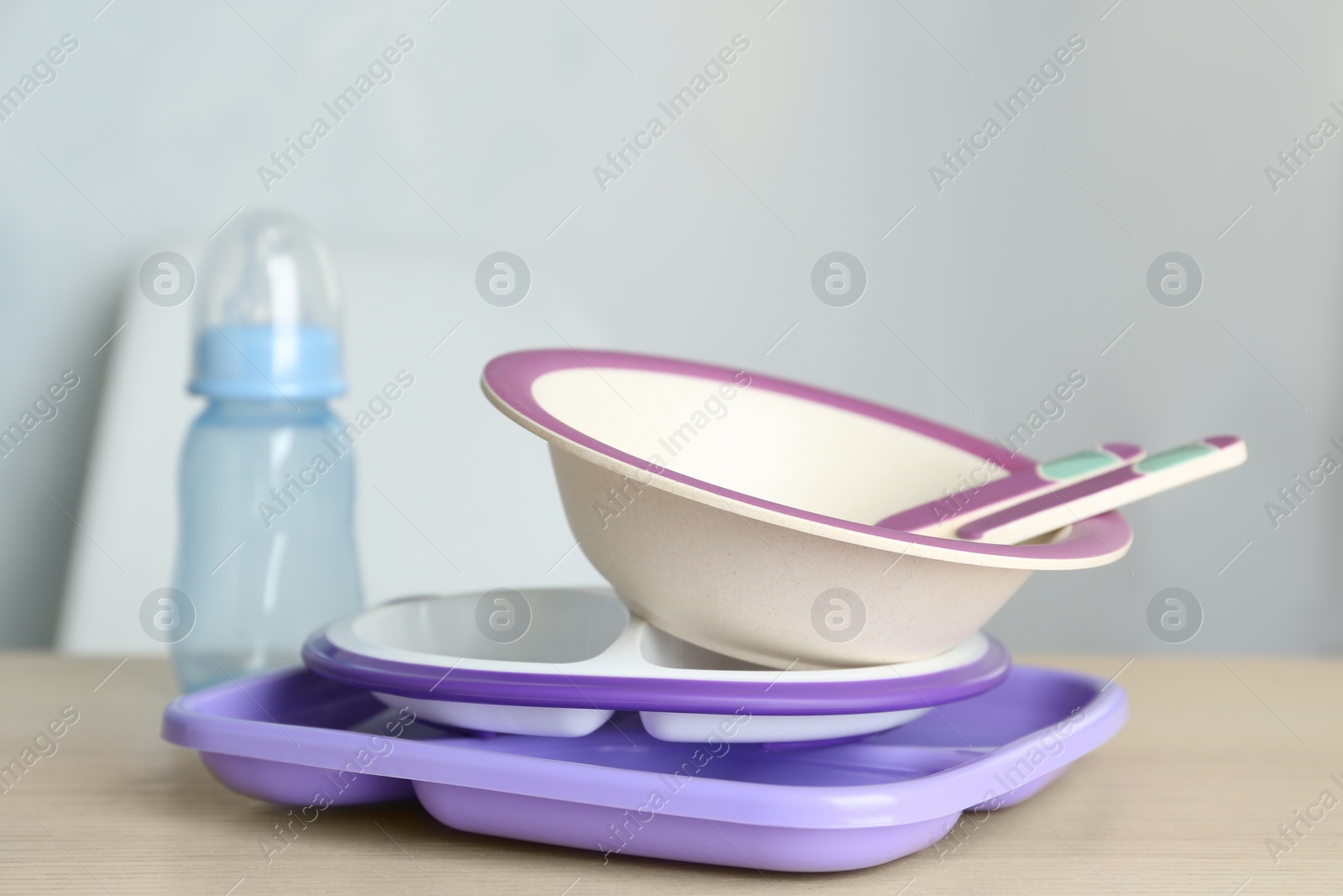 Photo of Set of plastic dishware on wooden table indoors. Serving baby food