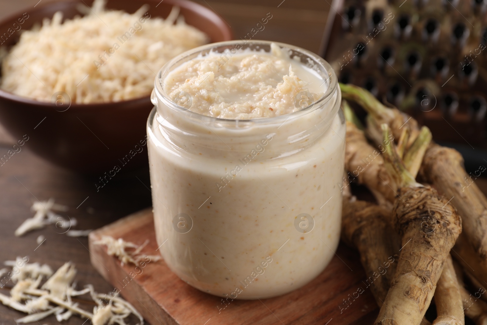 Photo of Spicy horseradish sauce in jar and roots on table, closeup