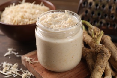 Spicy horseradish sauce in jar and roots on table, closeup