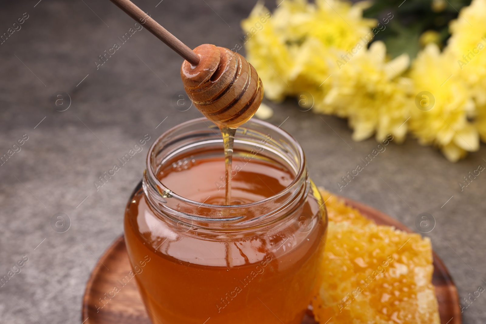 Photo of Pouring sweet golden honey from dipper into jar at grey table, closeup