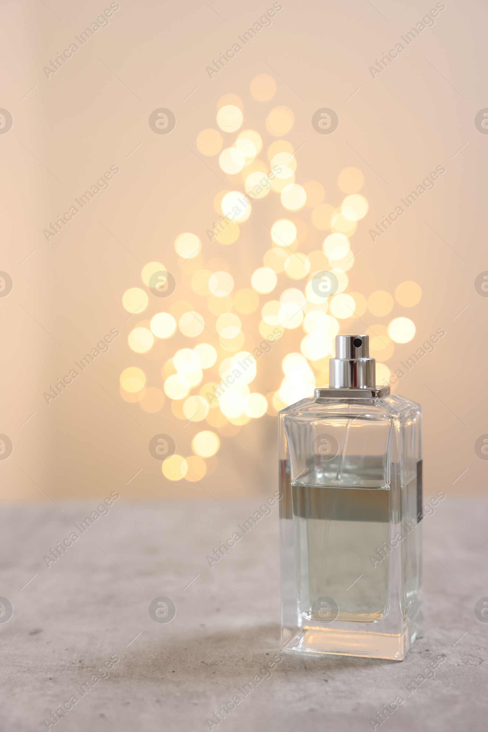 Photo of Bottle of perfume on table against beige background with blurred lights, space for text