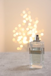 Photo of Bottle of perfume on table against beige background with blurred lights, space for text