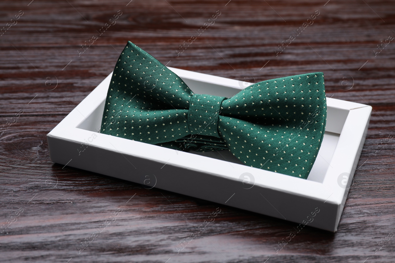 Photo of Stylish green bow tie with polka dot pattern in box on wooden table, closeup