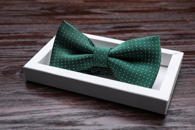 Stylish green bow tie with polka dot pattern in box on wooden table, closeup