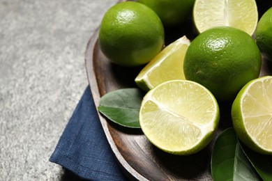 Fresh ripe limes and leaves on grey table, closeup. Space for text