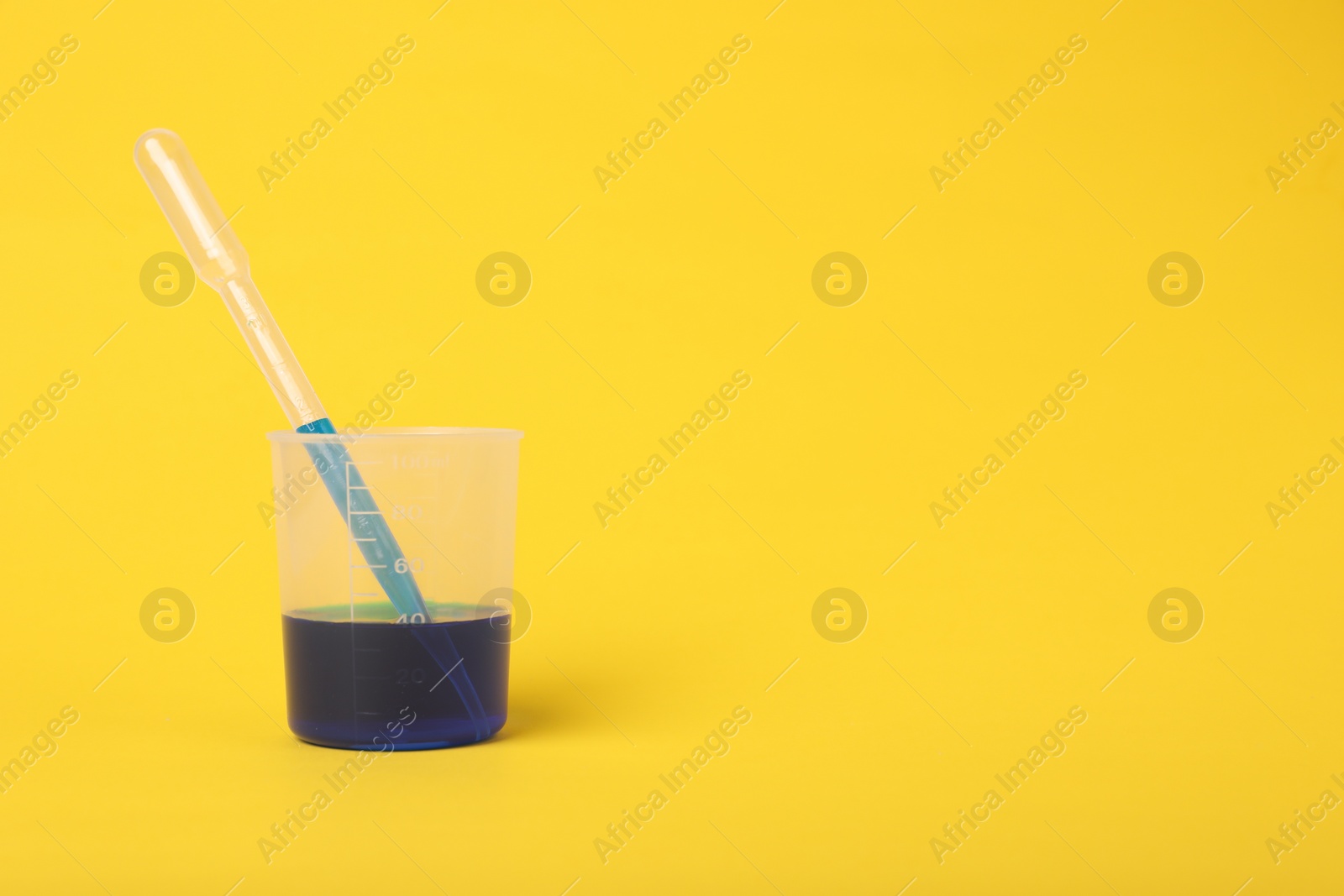 Photo of Beaker with liquid and stirring rod on yellow background, space for text. Kids chemical experiment toy