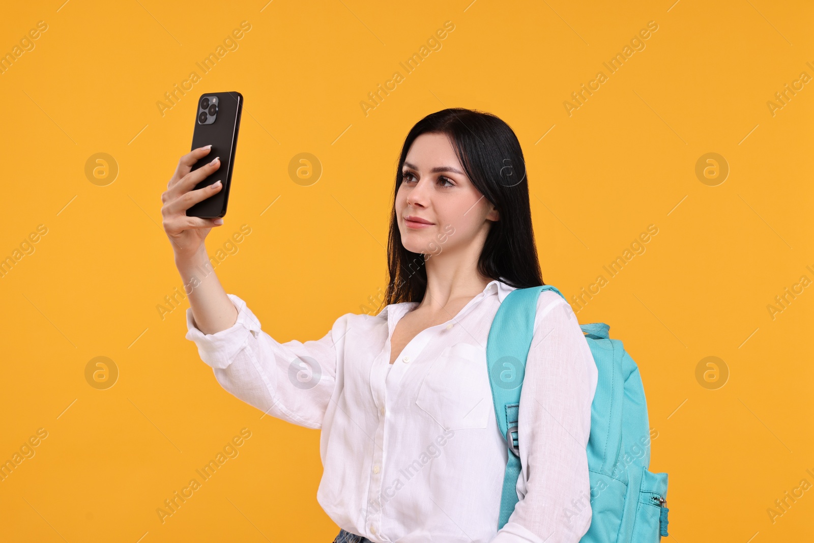Photo of Student with backpack taking selfie on yellow background