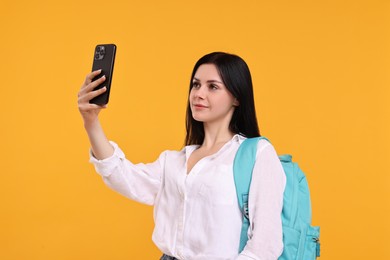 Student with backpack taking selfie on yellow background