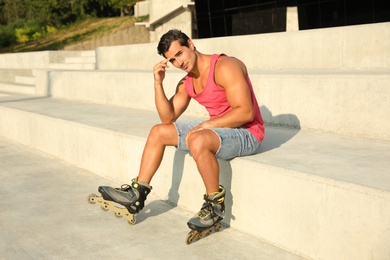 Photo of Handsome young man with inline roller skates sitting on stairs outdoors