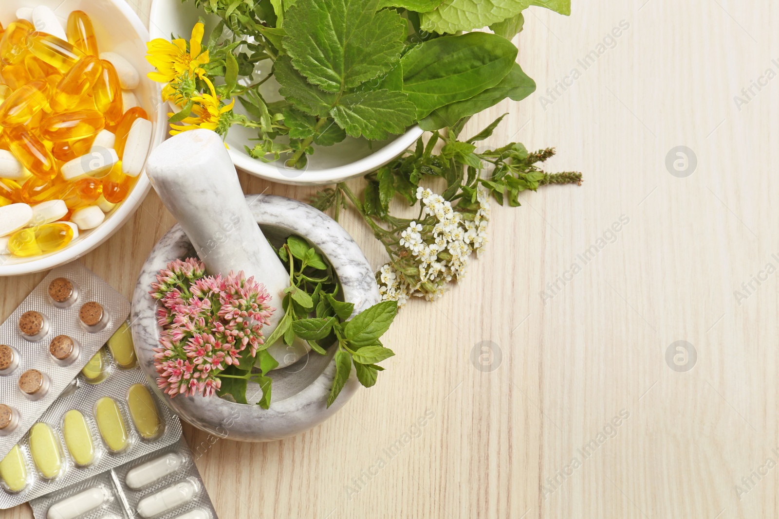 Photo of Mortar with fresh herbs and pills on wooden table, flat lay. Space for text