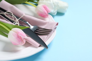 Stylish table setting with cutlery and tulips on light blue background, closeup. Space for text