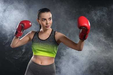 Photo of Beautiful woman wearing boxing gloves training in smoke on black background