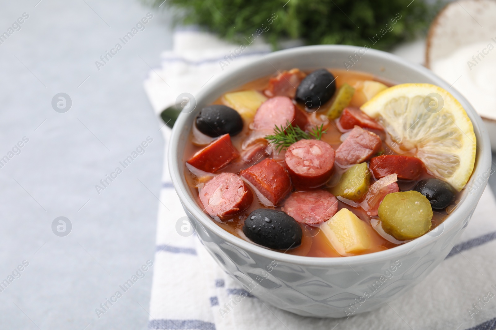 Photo of Meat solyanka soup with thin dry smoked sausages in bowl on grey table, closeup. Space for text