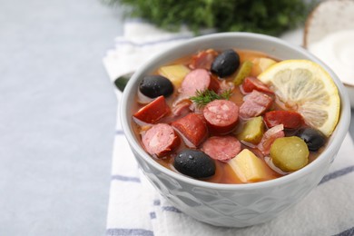 Photo of Meat solyanka soup with thin dry smoked sausages in bowl on grey table, closeup. Space for text