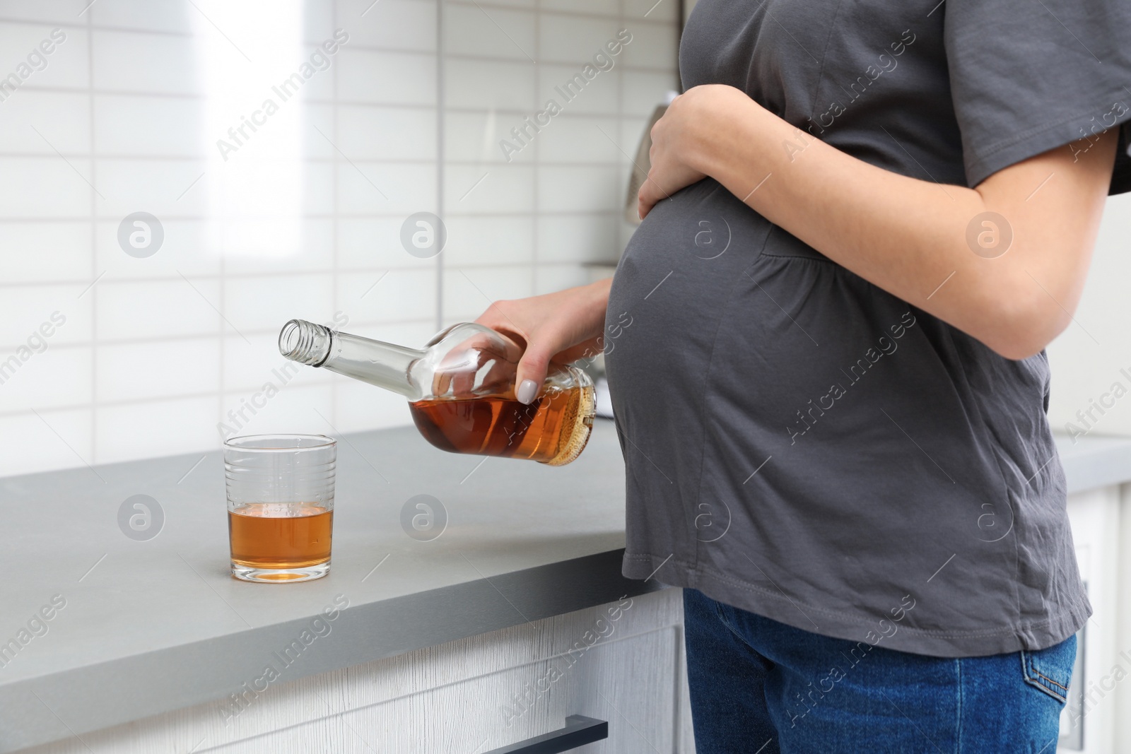 Photo of Future mother pouring alcohol drink from bottle into glass in kitchen, closeup. Bad habits during pregnancy