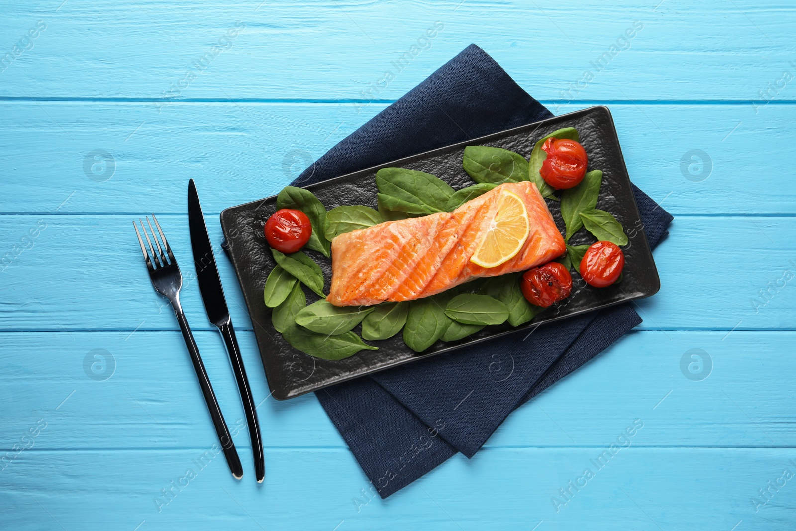 Photo of Tasty grilled salmon with tomatoes, spinach and lemon served on light blue wooden table, top view