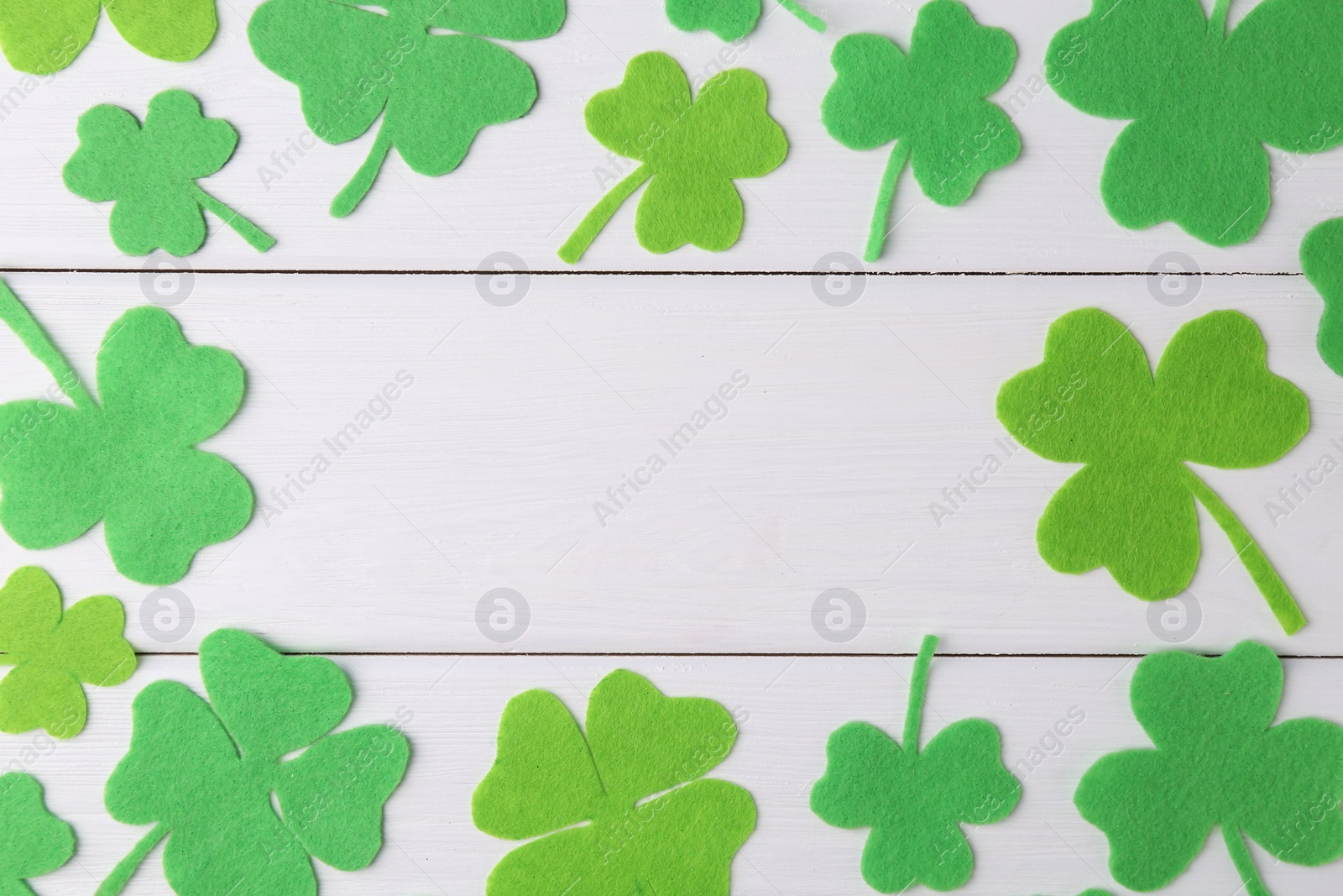 Photo of St. Patrick's day. Frame of green decorative clover leaves on white wooden table, flat lay. Space for text