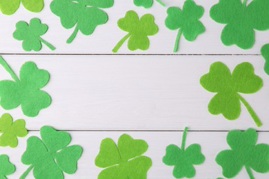 St. Patrick's day. Frame of green decorative clover leaves on white wooden table, flat lay. Space for text