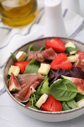 Tasty salad with brie cheese, prosciutto, strawberries and figs on white table