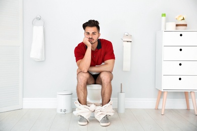 Young man sitting on toilet bowl at home