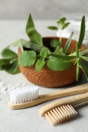 Photo of Toothbrushes and green herbs on light grey table, closeup