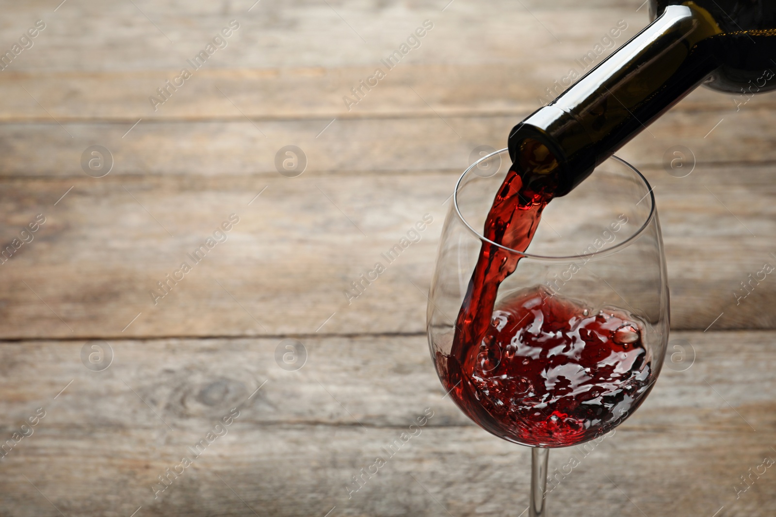 Photo of Pouring red wine from bottle into glass on wooden background. Space for text