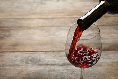 Pouring red wine from bottle into glass on wooden background. Space for text