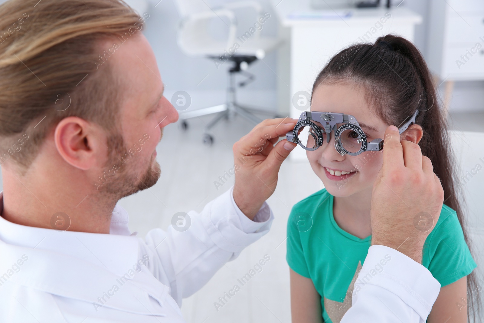 Photo of Children's doctor putting trial frame on little girl in clinic. Eye examination