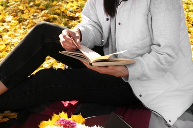 Photo of Woman reading book outdoors on autumn day, closeup