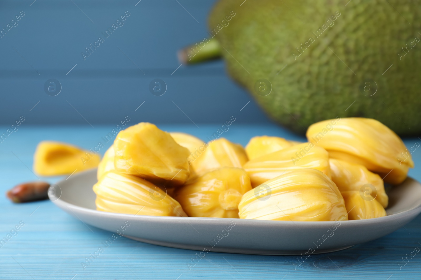 Photo of Delicious exotic jackfruit bulbs on light blue wooden table