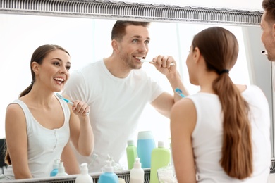 Photo of Young loving couple looking in mirror while brushing teeth indoors