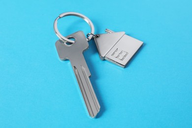 Photo of Metallic key with keychain in shape of house on light blue background