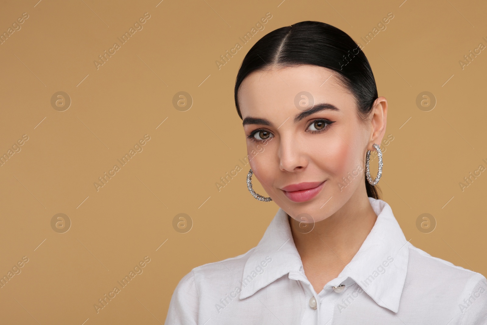 Photo of Beautiful young woman with elegant earrings on beige background. Space for text