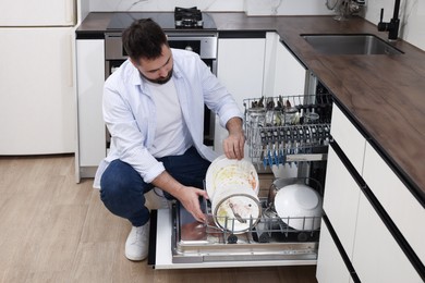 Photo of Man loading dishwasher with dirty plates indoors