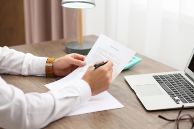 Photo of Man working with documents at wooden table in office, closeup