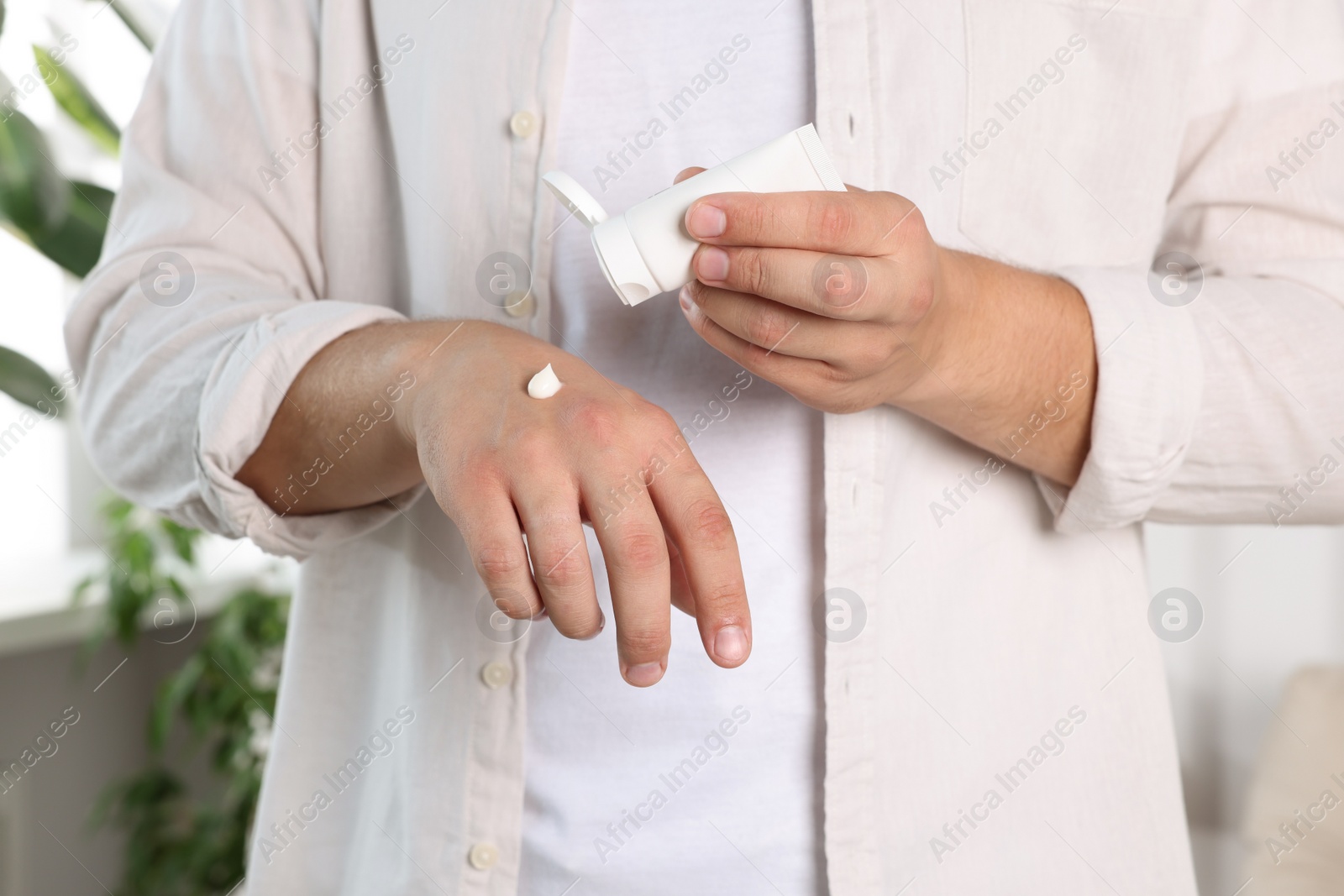 Photo of Man applying hand cream from tube at home, closeup