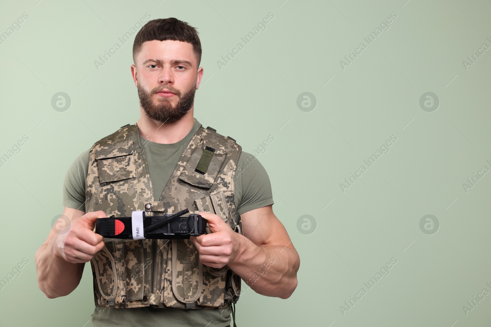 Photo of Soldier in military uniform holding medical tourniquet on light olive background. Space for text